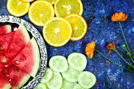 Colorful flatlay featuring sliced watermelon, oranges, and cucumbers on a blue background with flowers.